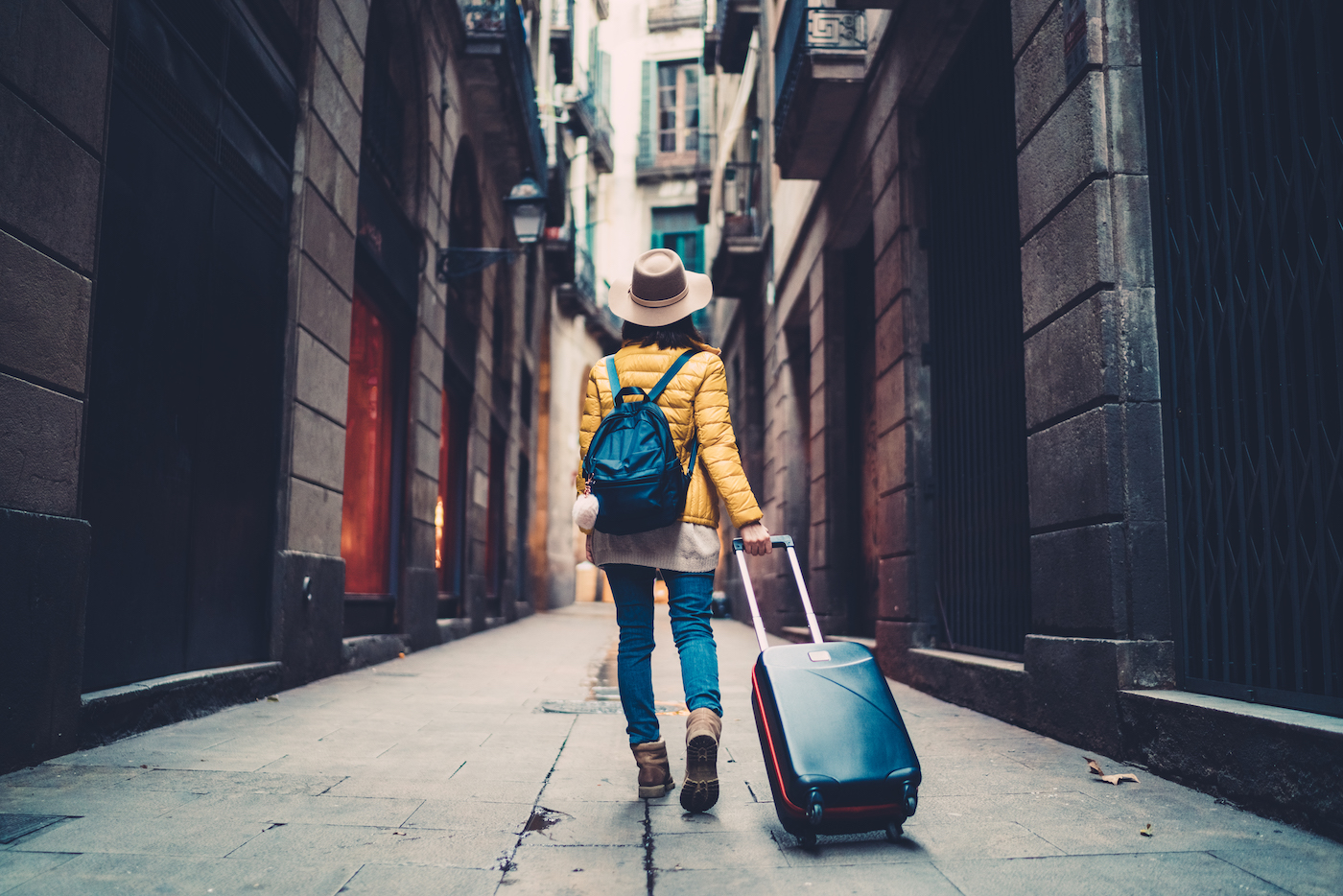 Person walking down a quiet city street pulling rolling luggage behind them representing what it means to be a worker in today’s work world.